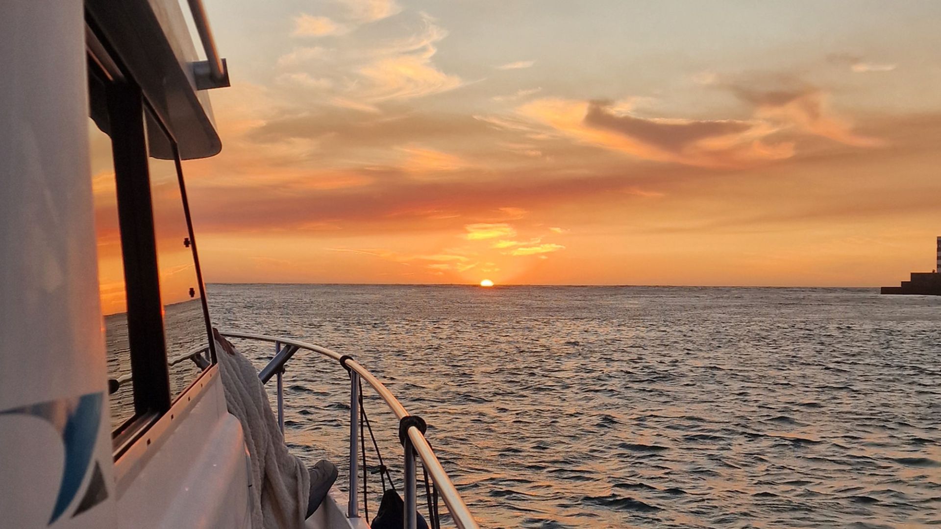 Boat on water at sunset with view of horizon and lighthouse in distance.