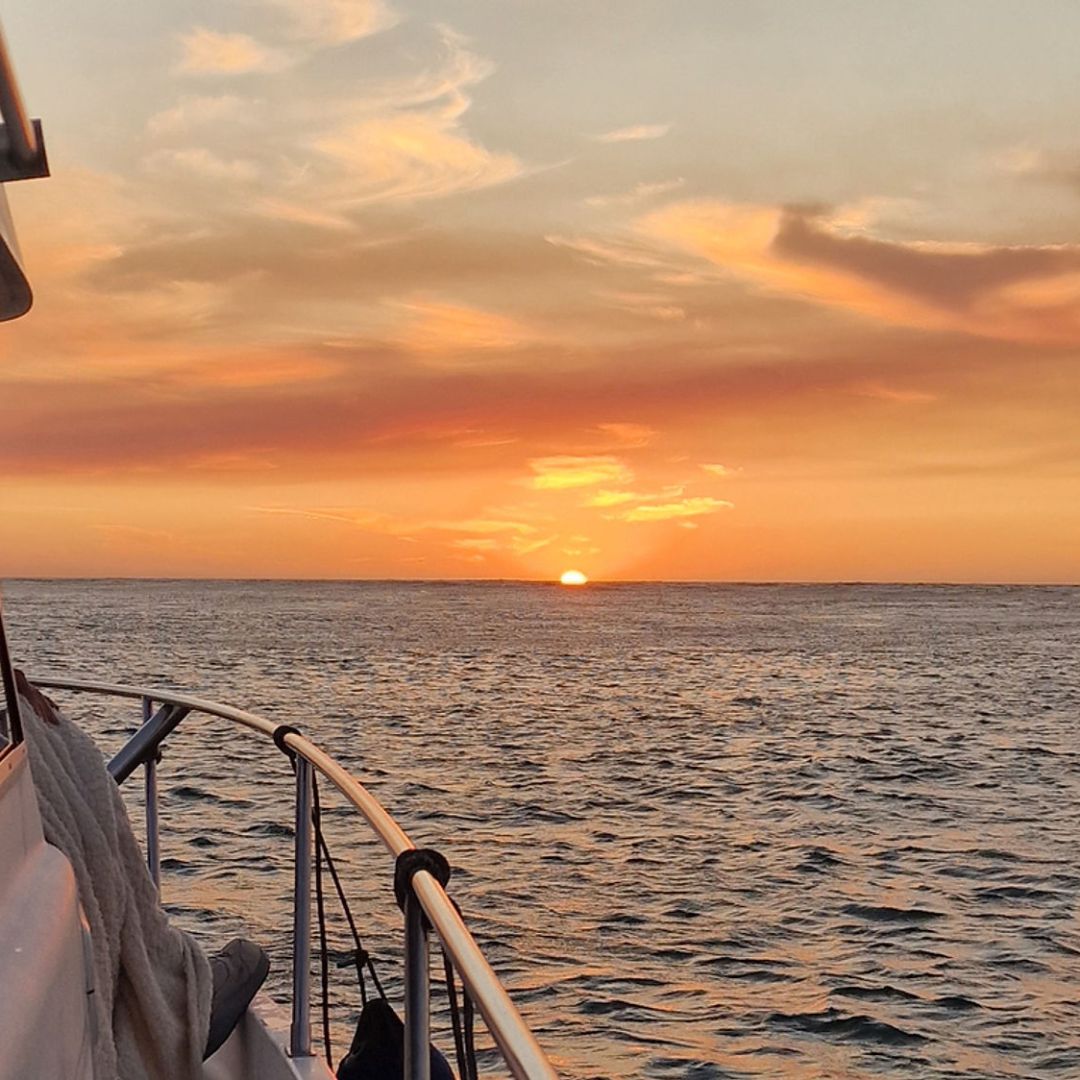 Boat at sea with a sunset and lighthouse in the distance.