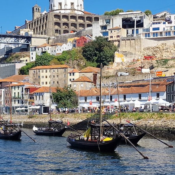 River with boats, bridge, and hillside buildings under blue sky.