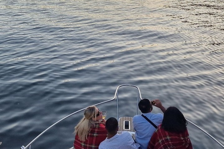 Three people sitting on a boat deck wrapped in blankets, looking out over calm water.