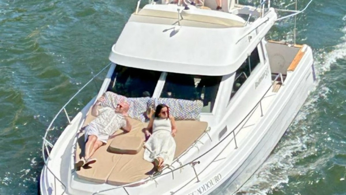 White boat on water with people relaxing and waving, including sunbathers on deck.