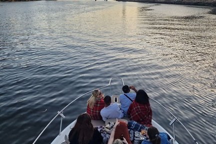 Group of people on a boat in a river heading towards a bridge at sunset.
