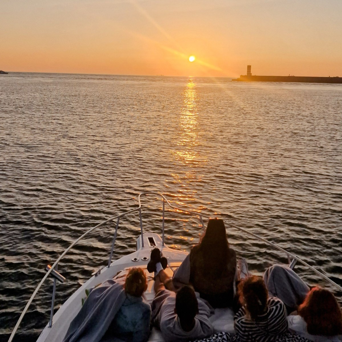People on a boat watching a sunset over the ocean with a distant shoreline.