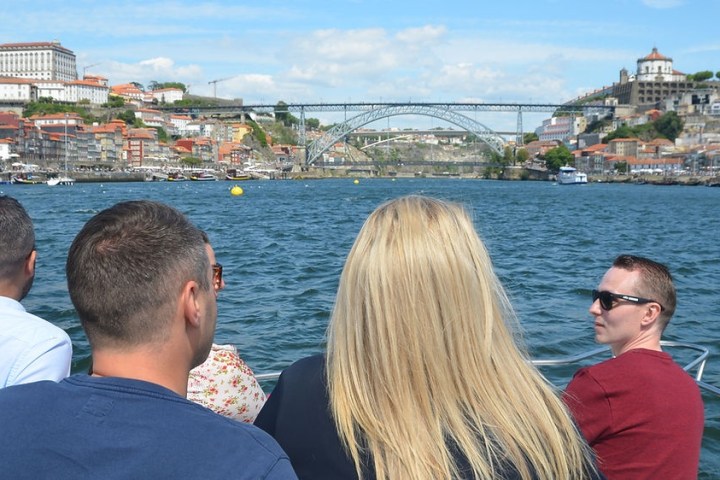 People on a boat cruising a river with cityscape and bridge view in the background.