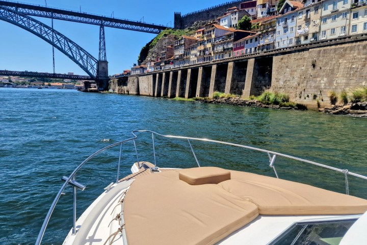 Boat on a river near a bridge and colorful hillside buildings in sunny weather.