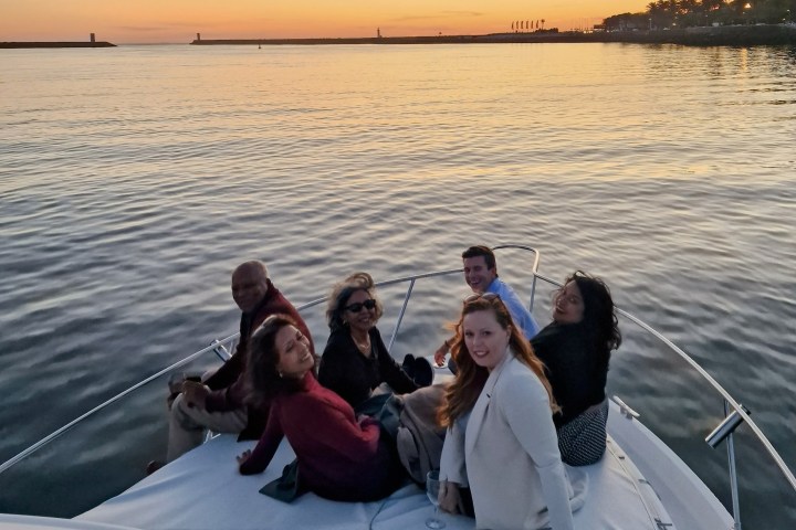 Six people sitting on a boat at sunset, smiling towards the camera.