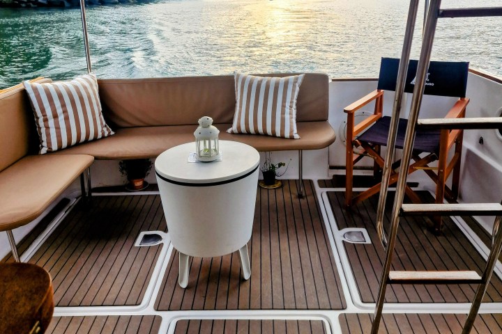 Boat deck with seating, striped cushions, table, lantern, and view of water at sunset.