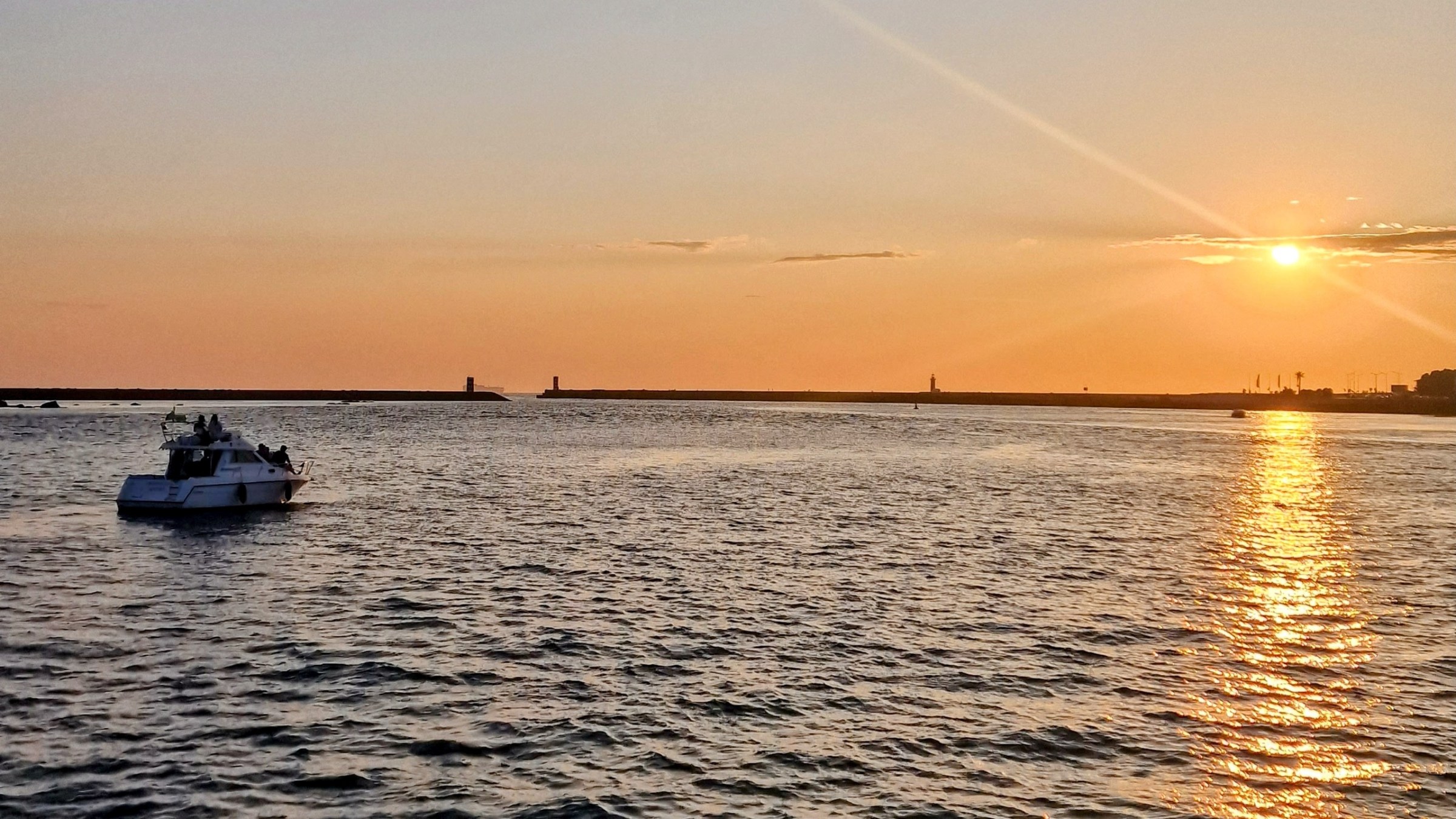 Boat on ocean at sunset with sun reflecting on water and horizon.