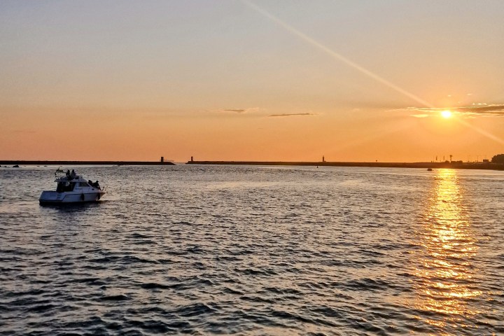Boat on ocean at sunset with sun reflecting on water and horizon.