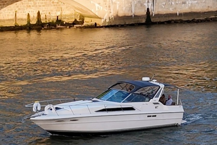Small white motorboat on a river near a stone bridge.