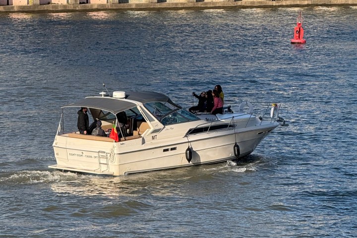 People on a white motorboat cruising on calm water near a dock.