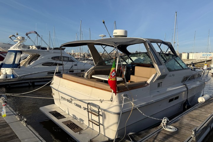 Motorboat docked in marina with Portuguese flag and clear sky.