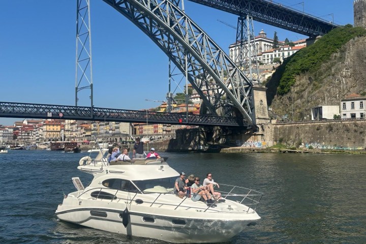 People on a white yacht under a large bridge on a sunny day.