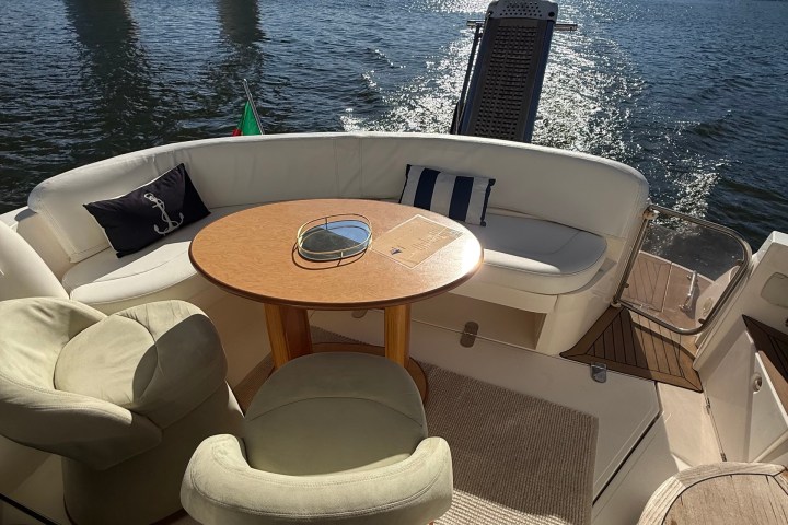 Sunny yacht deck with round table, cushioned seating, and water view.
