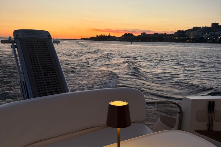Lamp on yacht table at sunset, overlooking ocean and distant shore.