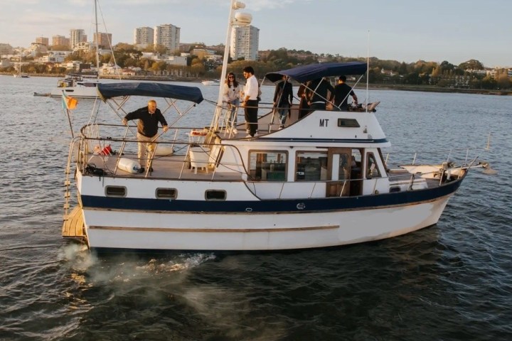 A small motorboat with people on deck, near a coastal city.