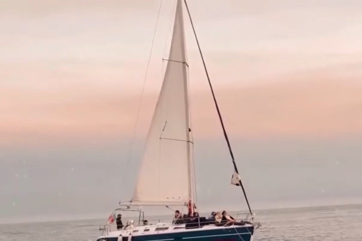 Sailboat with white sails on calm water at sunset.